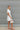 Side view of the Harmony Dress that features a white material, an asymmetrical neckline, a one shoulder short sleeve, a smocked waist, a flowy fit, and a mini length.