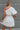 Back view of the Harmony Dress that features a white material, an asymmetrical neckline, a one shoulder short sleeve, a smocked waist, a flowy fit, and a mini length.