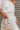 Frontal view of the Harmony Dress that features a white material, an asymmetrical neckline, a one shoulder short sleeve, a smocked waist, a flowy fit, and a mini length.