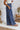 
Side view of the On Your Mark Pants that features a blue satin material, a high-rise fit, a thick waist band, a clasp and zipper front closure, side pockets, a wide leg fit, and two back pockets.
