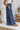 
Side view of the On Your Mark Pants that features a blue satin material, a high-rise fit, a thick waist band, a clasp and zipper front closure, side pockets, a wide leg fit, and two back pockets.
