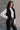 Side view of model wearing the Sienna Black Sherpa Cropped Zip-Up Vest which features black suede and black sherpa fabric, two front pocket slits, front zip up, collared neckline, cropped waist and sleeveless.