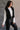 Side view of model wearing the Sienna Black Sherpa Cropped Zip-Up Vest which features black suede and black sherpa fabric, two front pocket slits, front zip up, collared neckline, cropped waist and sleeveless.