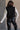 Back view of model wearing the Sienna Black Sherpa Cropped Zip-Up Vest which features black suede and black sherpa fabric, two front pocket slits, front zip up, collared neckline, cropped waist and sleeveless.