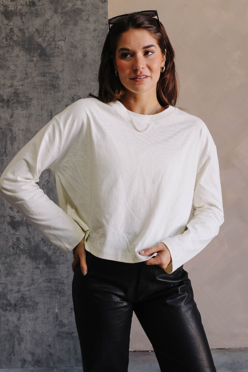 Front view of model wearing the Nikole Cream Cropped Long Sleeve Sweatshirt which features cream cotton fabric, cropped waist, round neckline and long sleeves.
