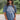 Front view of model wearing the Ford Graphic Tee that has dusty blue cotton fabric, round neckline and short sleeves. Graphic says "FORD" "MOTOR CO." "DETROIT" in white lettering. Graphic has a tire with wings in white. 