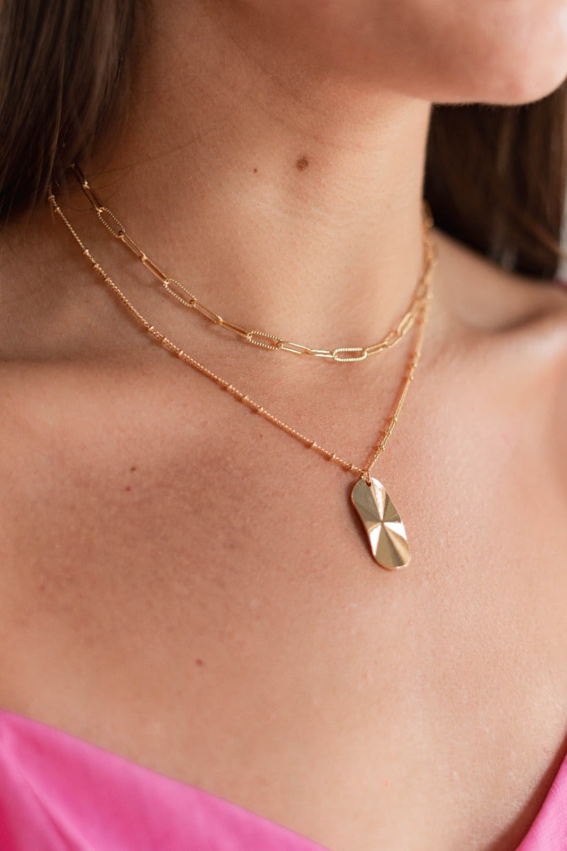 Close up view of model wearing the Double Trouble Chain Necklace which features a double gold chain link with a gold chain link and hammered medallion.