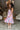 Full body view of model wearing the In My Favor Midi Dress which features a hot pink, light pink, green, blue and lavender color block pattern, tiered ruffle details, a pink skirt lining, a square neckline, adjustable straps, a smocked back, and a monochr