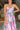 Close up view of model wearing the In My Favor Midi Dress which features a hot pink, light pink, green, blue and lavender color block pattern, tiered ruffle details, a pink skirt lining, a square neckline, adjustable straps, a smocked back, and a monochro