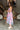 Side view of model wearing the In My Favor Midi Dress which features a hot pink, light pink, green, blue and lavender color block pattern, tiered ruffle details, a pink skirt lining, a square neckline, adjustable straps, a smocked back, and a monochromati