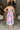 Full body back view of model wearing the In My Favor Midi Dress which features a hot pink, light pink, green, blue and lavender color block pattern, tiered ruffle details, a pink skirt lining, a square neckline, adjustable straps, a smocked back, and a mo