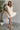Full body front view of model wearing the One More Time Dress that has cream sheer fabric, a ruffled stripe design, a bubble hem, cream lining, a plunge neckline, ruffle straps, an open back and a monochromatic back zipper with a hook closure