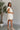 Full body side view of model wearing the One More Time Dress that has cream sheer fabric, a ruffled stripe design, a bubble hem, cream lining, a plunge neckline, ruffle straps, an open back and a monochromatic back zipper with a hook closure