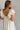 Back view of model wearing the One More Time Dress that has cream sheer fabric, a ruffled stripe design, a bubble hem, cream lining, a plunge neckline, ruffle straps, an open back and a monochromatic back zipper with a hook closure