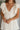 Close front view of model wearing the One More Time Dress that has cream sheer fabric, a ruffled stripe design, a bubble hem, cream lining, a plunge neckline, ruffle straps, an open back and a monochromatic back zipper with a hook closure