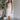 Front view of model wearing the Everlasting Love Mini Dress which features white sheer fabric with white floral embroidery, white tulle lining, tan lining, mini length, a halter neckline with a tie closure, and an open back with button closures.