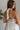 Close upper back view of model wearing the Everlasting Love Mini Dress which features white sheer fabric with white floral embroidery, white tulle lining, tan lining, mini length, a halter neckline with a tie closure, and an open back with button closures