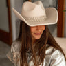 Front view of model wearing the Majestic Cowgirl Hat in Ivory which features cowboy-shaped hat, ivory fabric and rhinestone dangle details.