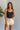 Front view of model wearing the Billie Cropped Denim Tank that has black acid wash fabric, a cropped waist, a square neckline, a sleeveless design, and a monochromatic back zipper with a hook closure.