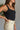 Close side view of model wearing the Billie Cropped Denim Tank that has black acid wash fabric, a cropped waist, a square neckline, a sleeveless design, and a monochromatic back zipper with a hook closure.