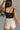 Back view of model wearing the Billie Cropped Denim Tank that has black acid wash fabric, a cropped waist, a square neckline, a sleeveless design, and a monochromatic back zipper with a hook closure.
