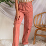 Front view of model wearing the Street Views Cargo Pants which features mauve fabric, white contrast stitching, front pockets, side cargo pockets, back cargo pockets, a drawstring hem at the ankles, an elastic waistband with drawstring ties, and wide legs
