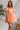Front view of model wearing the Into The Sunset Dress which features peach fabric with peach lining, square neckline, short puff sleeves, a smocked back and a monochromatic side zipper with a hook closure.