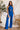 Front view of model wearing the Get On My Level Jumpsuit that has royal blue fabric, a front key hole , a halter neck with button closures, a sleeveless design, an open back, a back zipper with a hook closure, and flare pant legs.