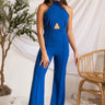 Front view of model wearing the Get On My Level Jumpsuit that has royal blue fabric, a front key hole , a halter neck with button closures, a sleeveless design, an open back, a back zipper with a hook closure, and flare pant legs.