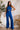 Front view of model wearing the Get On My Level Jumpsuit that has royal blue fabric, a front key hole , a halter neck with button closures, a sleeveless design, an open back, a back zipper with a hook closure, and flare pant legs.