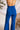 Close back view of model wearing the Get On My Level Jumpsuit that has royal blue fabric, a front key hole , a halter neck with button closures, a sleeveless design, an open back, a back zipper with a hook closure, and flare pant legs.