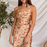 Front view of model wearing the Be Free Floral Dress which features satin fabric with rust orange, tan, light grey, taupe and olive floral print, mini length, a scooped neckline, and an open back with corset ties.