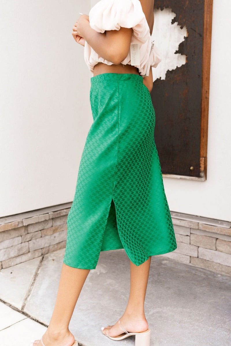 Side view of the Flow With Me Midi Skirt that features a green monochromatic houndstooth pattern, an elastic waistband, a side slit, and a midi length.