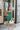 Frontal view of the Something Like That Dress that features a teal green satin material, a cowl neckline with cups at the bust, a sleeveless design with thin adjustable straps, a waist cut-out, an elastic waistline, and a criss-cross strap back