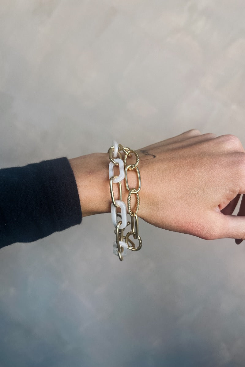 Close up view of model wearing the Nessa Gold and White Tortoise Chain Bracelet which features brushed gold chain, brushed gold braided chain and white chain linked together.