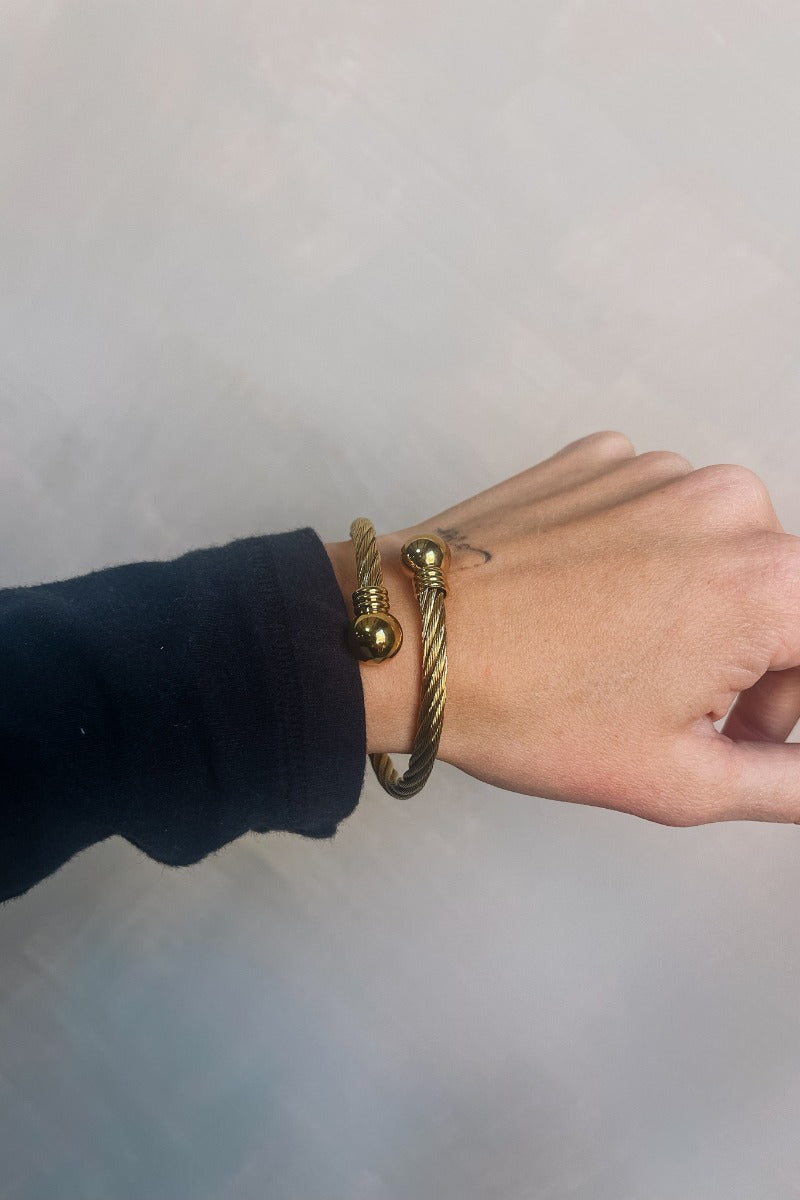 Close up view of model wearing the Lucy Gold Roped Bangle which features gold braided band with gold bead stoppers.
