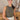 Front view of model wearing the Call It Even Bodysuit, that features stretchy olive fabric, a round neckline, and a thong bottom with hook closures. Worn with white jeans.