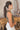 Side view of model wearing the Call It Even Bodysuit, that features stretchy olive fabric, a round neckline, and a thong bottom with hook closures. Worn with white jeans.