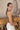 Side view of model wearing the Call It Even Bodysuit, that features stretchy olive fabric, a round neckline, and a thong bottom with hook closures. Worn with white jeans.