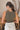 Back view of model wearing the Call It Even Bodysuit, that features stretchy olive fabric, a round neckline, and a thong bottom with hook closures. Worn with white jeans.