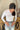 Front view of model wearing the On The Daily Bodysuit, that has white textured fabric, a high neck with lettuce trim, long sleeves with lettuce trim, and a thong bottom with hook closures. Worn with jeans.
