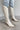 Frontal/ side view of the Going Places Boot that features a white colored western style boot, featuring a white leather upper, western inspired embroidery, an almond toe, a 2" stacked heel, pull-on tabs for easy entry, and a side zipper.