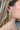 Close view of model wearing the Going Glam Earrings feature post backs with criss-crossed gold tassels.
