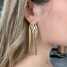 Close view of model wearing the Going Glam Earrings feature post backs with criss-crossed gold tassels.