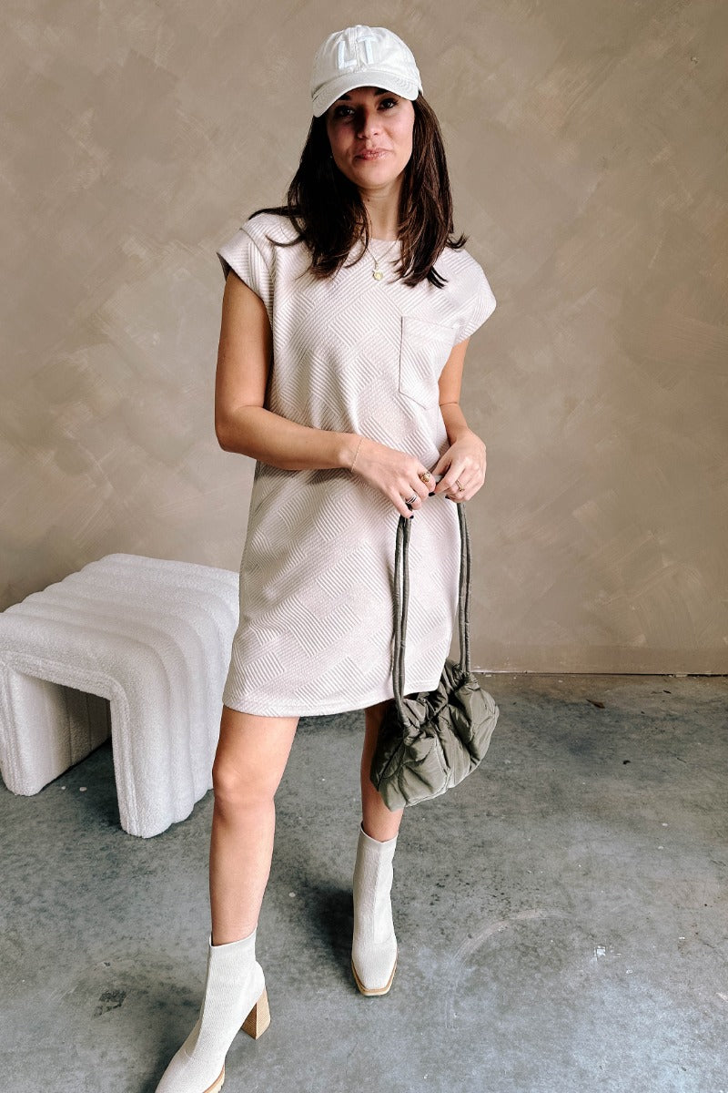 Full body view of model wearing the Palmer Light Taupe Short Sleeve Dress which features light taupe knit fabric, monochrome block stripe design, mini length, two slit side pockets, left front chest pocket, round neckline and sleeveless.