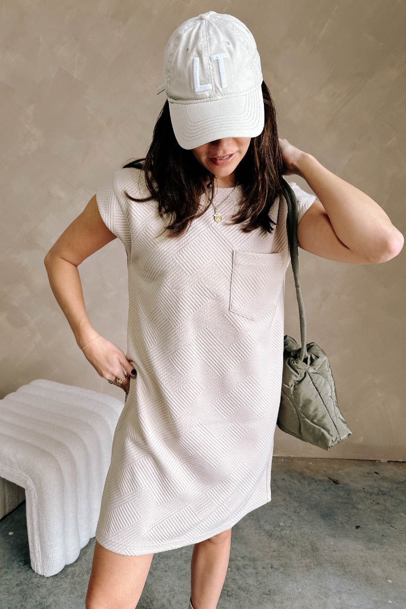 Front view of model wearing the Palmer Light Taupe Short Sleeve Dress which features light taupe knit fabric, monochrome block stripe design, mini length, two slit side pockets, left front chest pocket, round neckline and sleeveless.