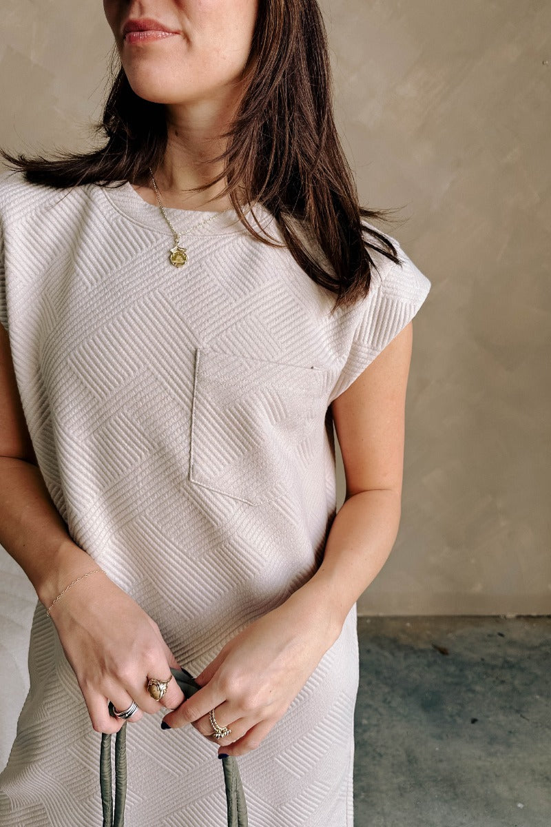 Close up view of model wearing the Palmer Light Taupe Short Sleeve Dress which features light taupe knit fabric, monochrome block stripe design, mini length, two slit side pockets, left front chest pocket, round neckline and sleeveless.