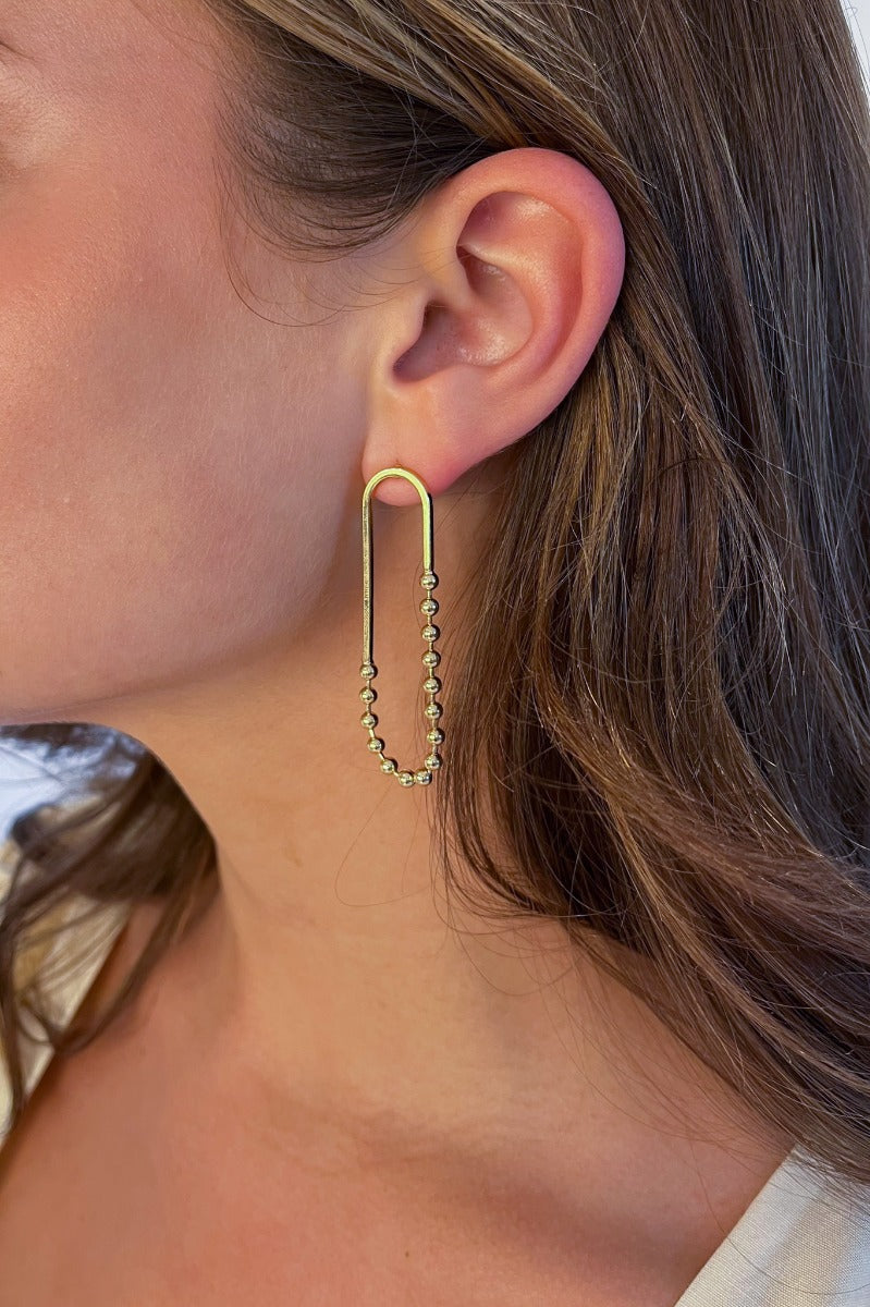 Side view of model wearing the Small Things Beaded Earring which features gold ovals with gold beads.