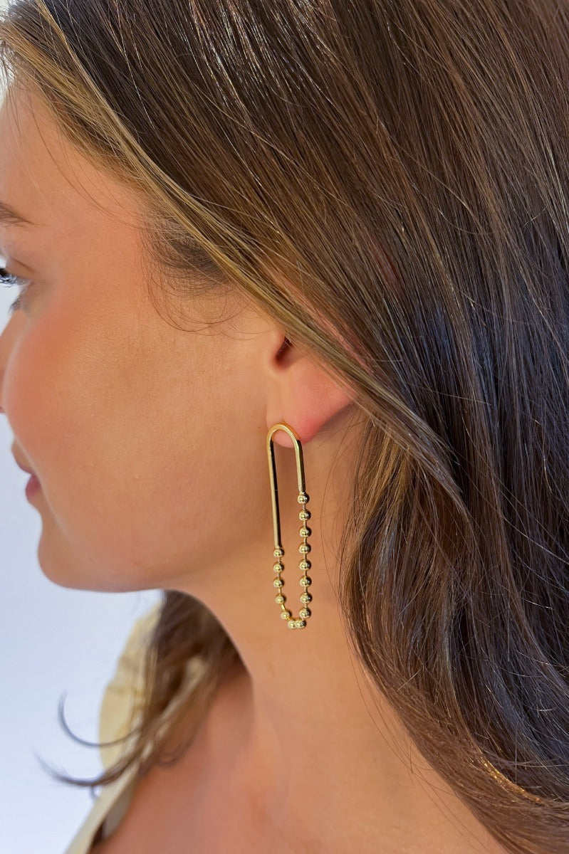 Side view of model wearing the Small Things Beaded Earring which features gold ovals with gold beads.