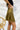 Side view of the Make It Mine Skort that features a moss green silk material, a high-rise fit, an elastic waist band, a flowy ruffle bottom, a shorts lining, and a back zipper closure.